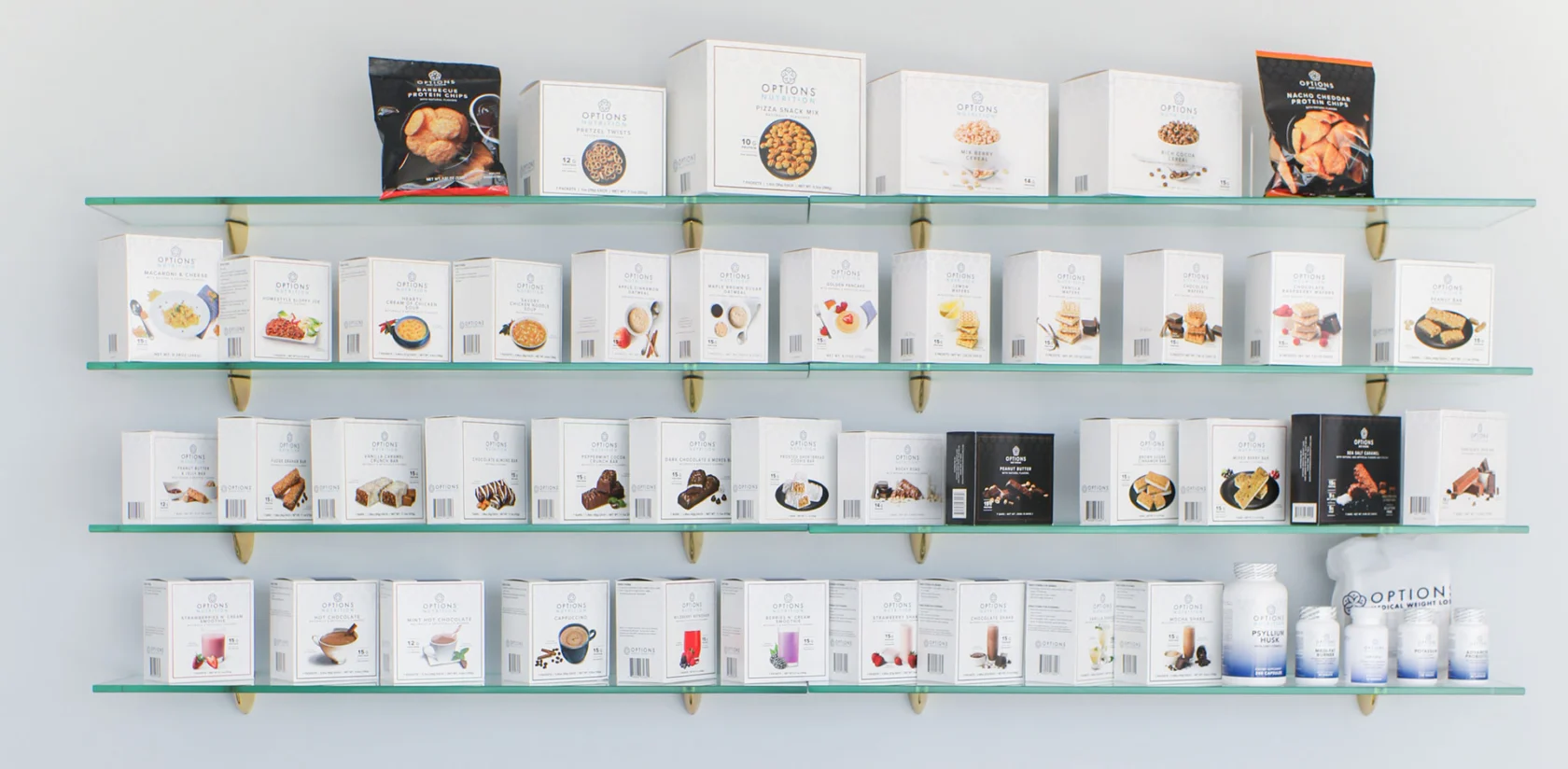 Display of various packaged food items and drinks on three glass shelves. Packaging features images of the contents, including snacks and drinks.