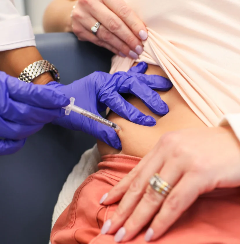 A person receives an injection in the abdomen from a healthcare professional wearing blue gloves.