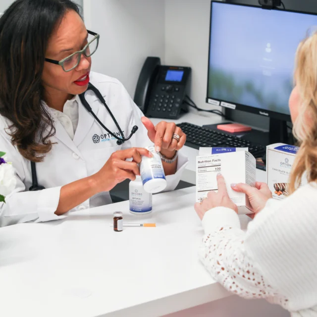 A doctor discusses skincare products with a patient at a desk in a medical office.